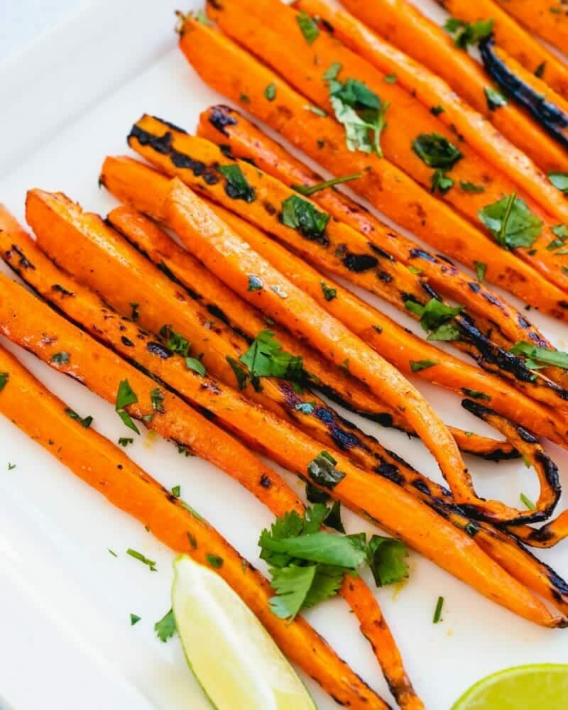 Grilled carrots lined up and sprinkled with a green herb and lime wedges