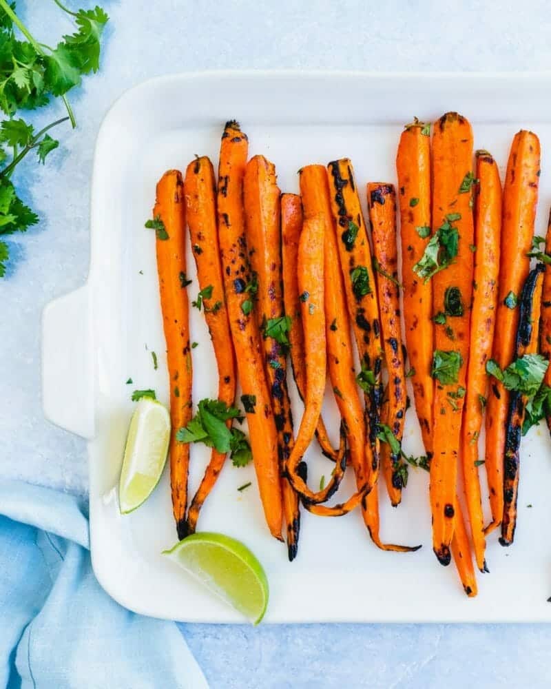 Grilled carrots lined up and sprinkled with a green herb and lime wedges
