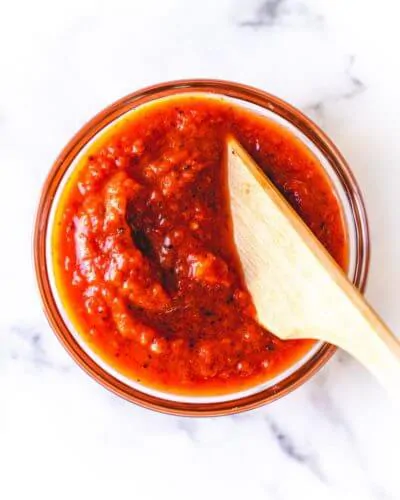 Homemade pizza sauce in a small bowl with a wooden cooking utensil