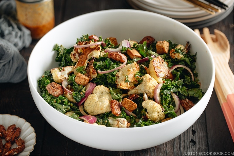 A large white bowl containing Roasted Cauliflower Kale Salad tossed with Miso Tahini Dressing.