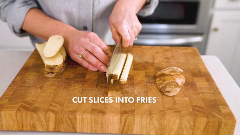 A woman is cutting the thin slices of potatoes into fry shaped slices on a cutting board. It says, "Cut slices into fries."