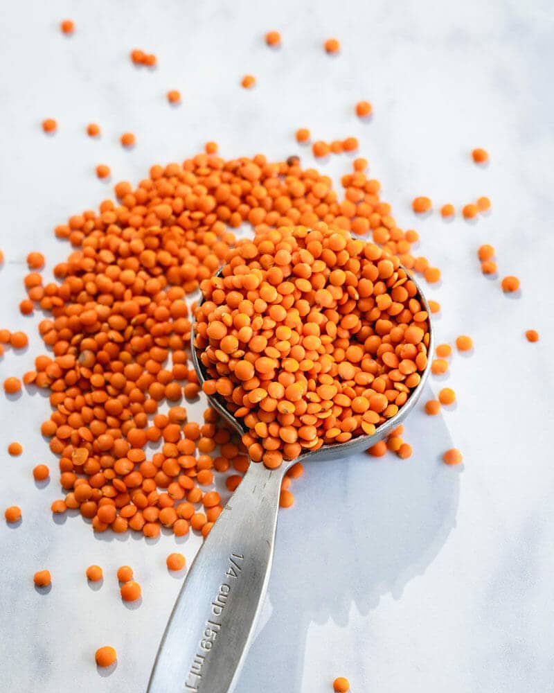 Red lentils in a ¼ cup measuring cup and spilling over the side onto a surface