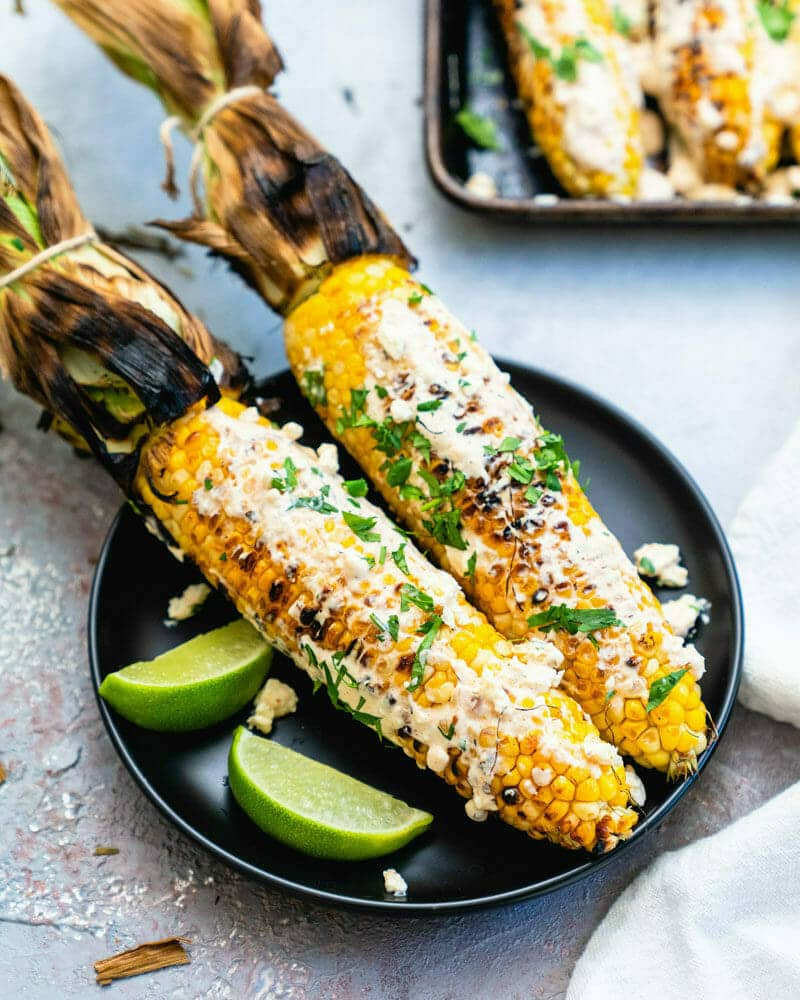 Elote (Mexican Street Corn) sitting on a plate with a couple of limes