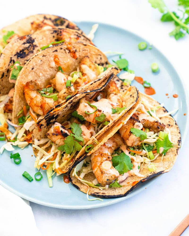 Several grilled shrimp tacos lined up on a plate and garnished with cilantro