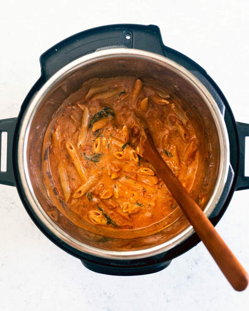 An Instant Pot full of creamy pasta and sauce mix, with a wooden spoon