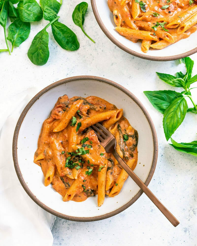 Two bowls of creamy Instant Pot pasta wtih some fresh basil on the counter nearby