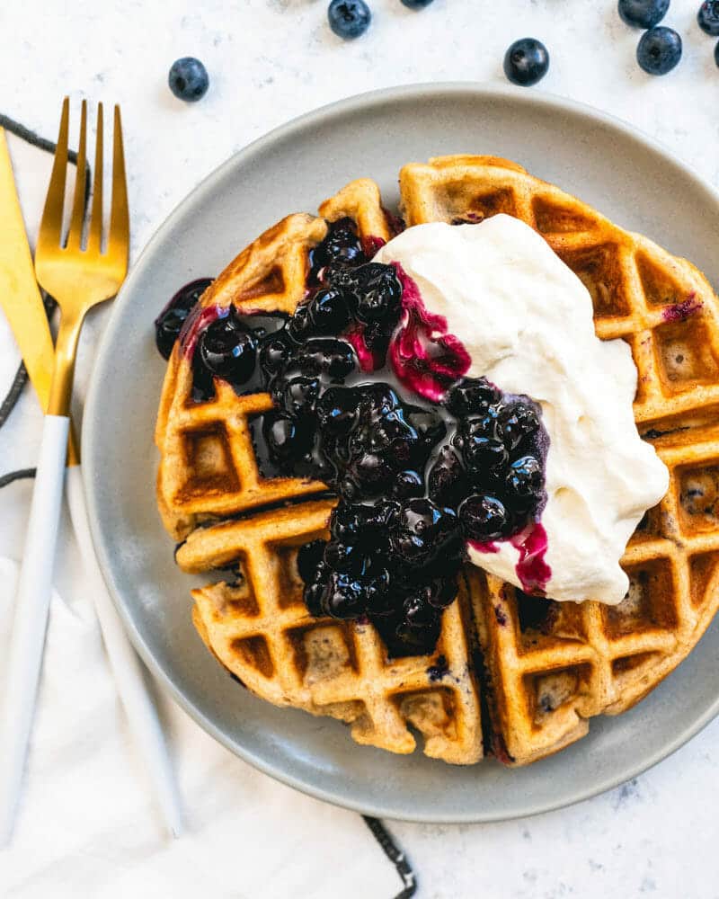 Blueberry waffle on a plate, topped with whipped cream and blueberry sauce