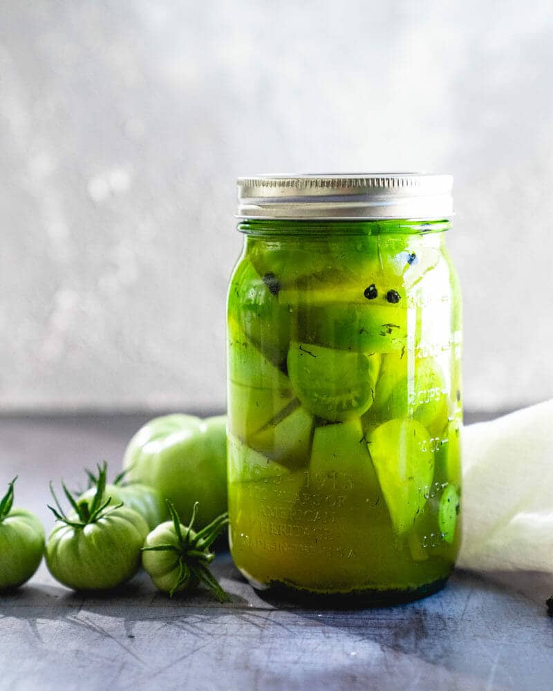 Pickled green tomatoes in jar with green tomatoes next to the jar