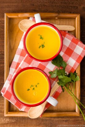 Mug cups containing kabocha soup served on a wooden tray.