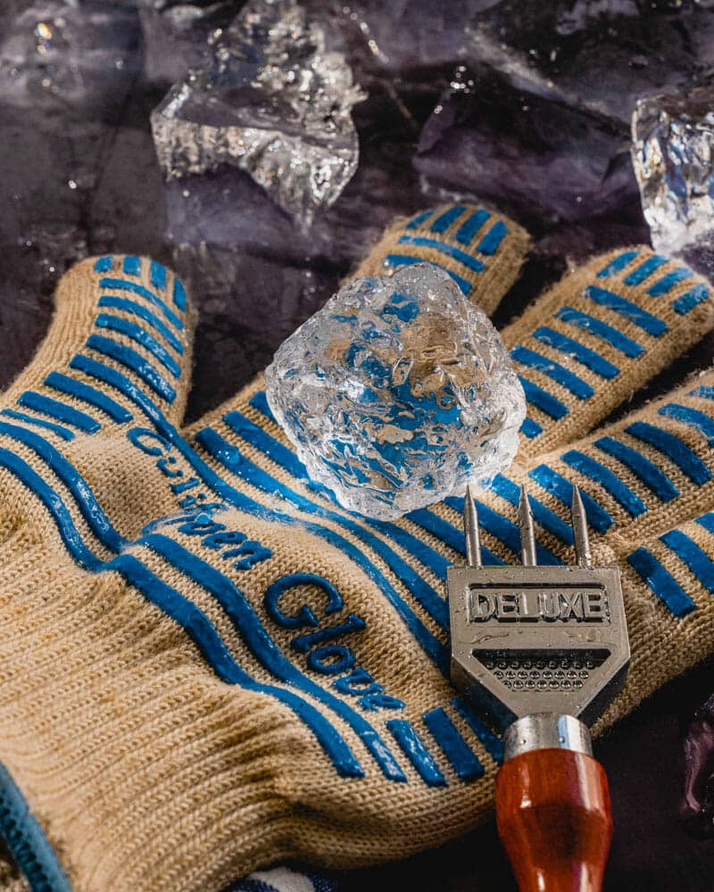 A gloved hand holding broken clear ice and shaping it with an ice pick