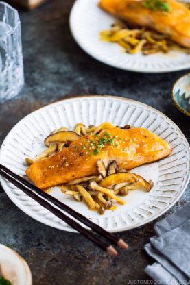 A white plate containing Miso Butter Salmon served with saut&eacute;ed shiitake and shimeji mushrooms.