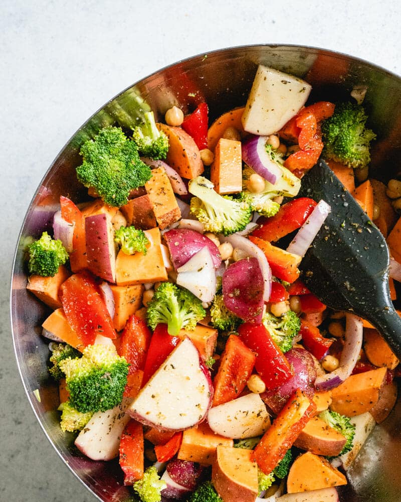 A bowl of mixed veggies, including sweet potatoes, red onions, broccoli, red peppers, and chickpeas