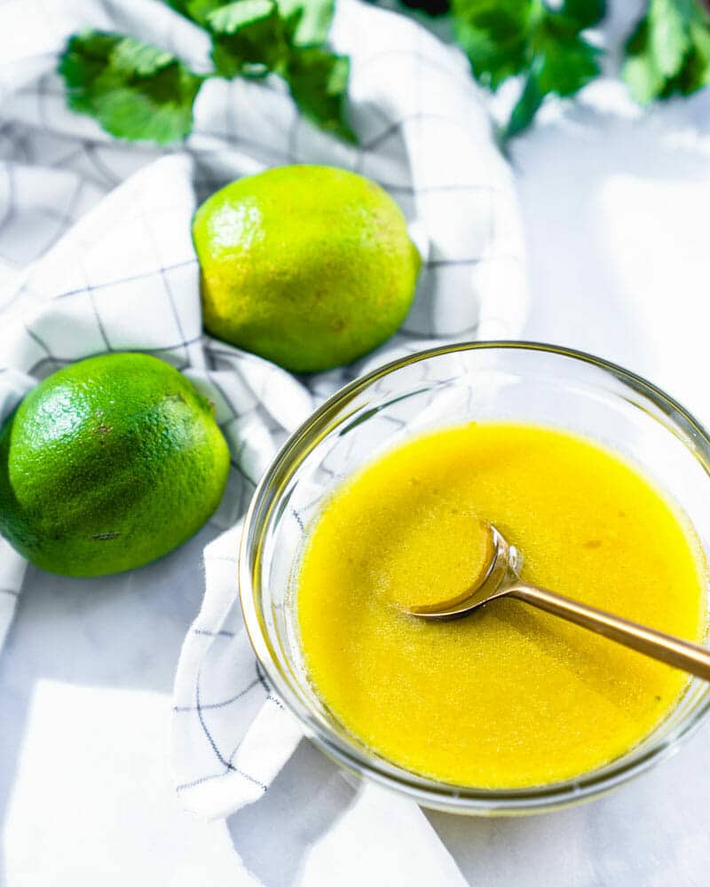 Lime vinaigrette in a clear glass bowl, with two limes sitting next to it