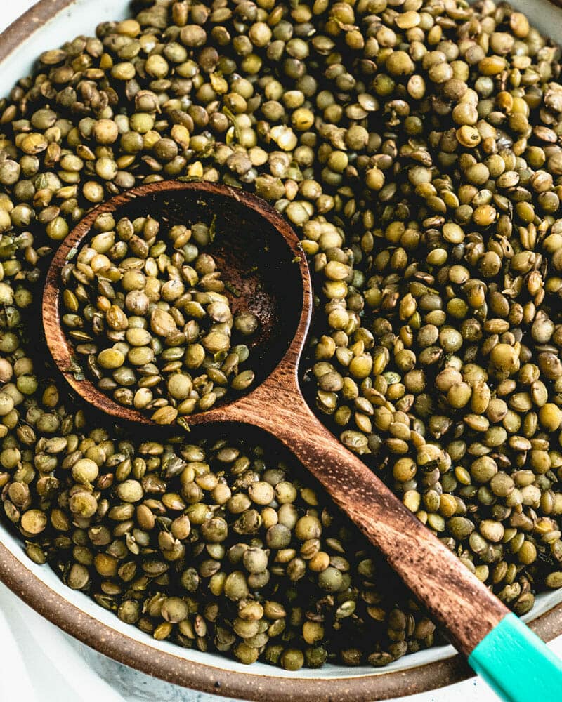 French lentils withh a small brown bowl with a handle sitting on top of them and containing more lentils