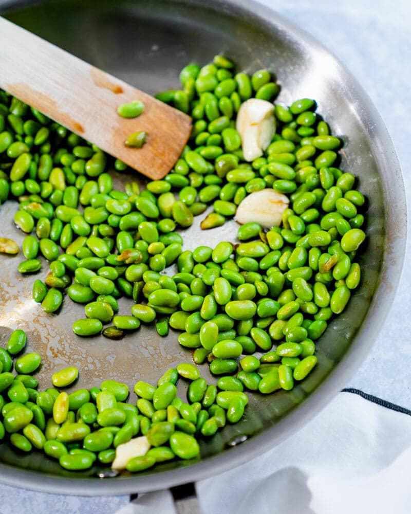 Shelled edamame in skillet being cooked with garlic