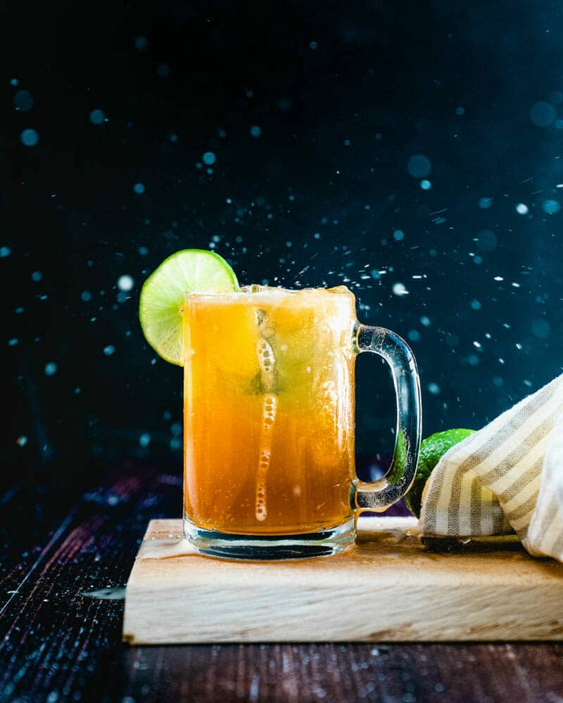 Beer margarita in a beer mug with a lime on the side, sitting on a cutting board