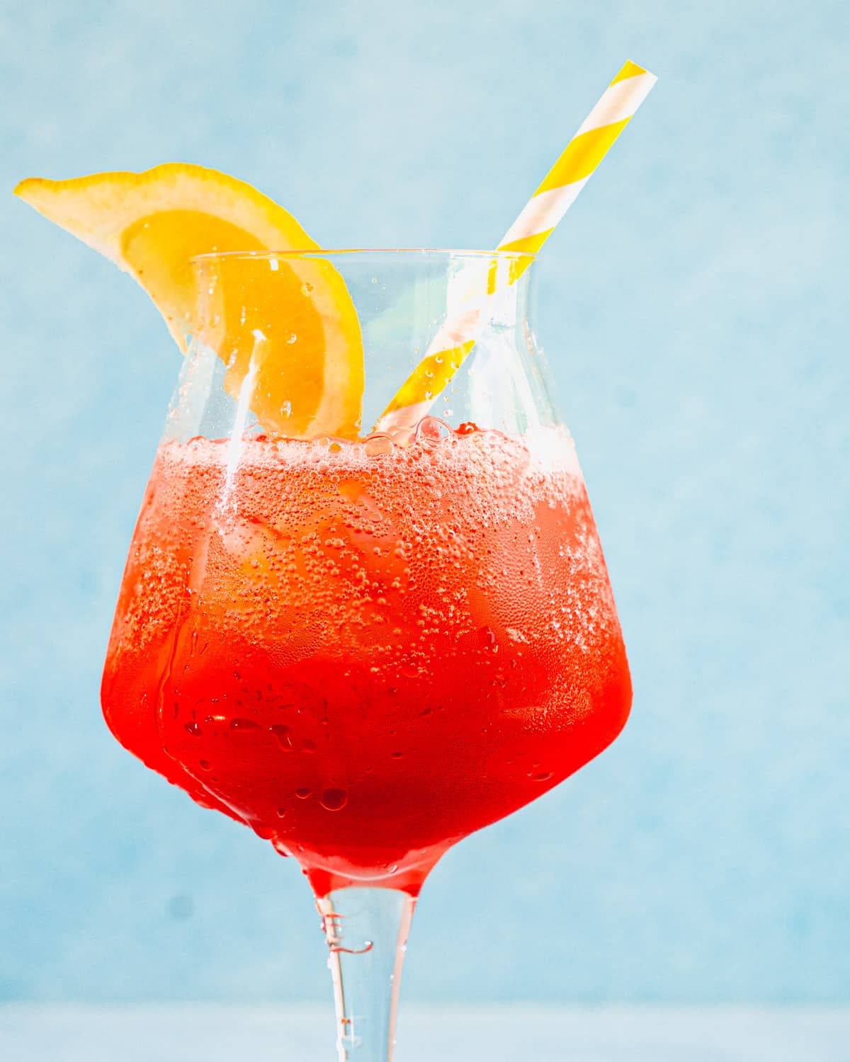 Campari spritz in a glass with a lemon wedge and a straw.