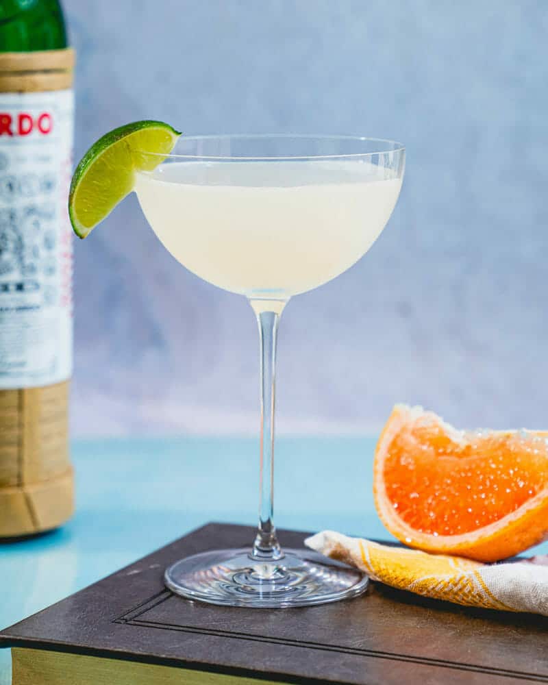 Hemingway daiquiri in a long-stemmed cocktail glass with a lime, sitting on a table with an orange slice