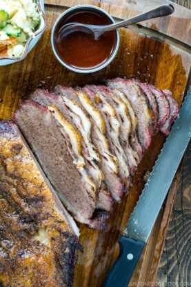 Smoked A5 Japanese wagyu brisket on a wood cutting board next to bbq sauce and potato salad | Easy Japanese Recipes at fancyfoodsshow.com