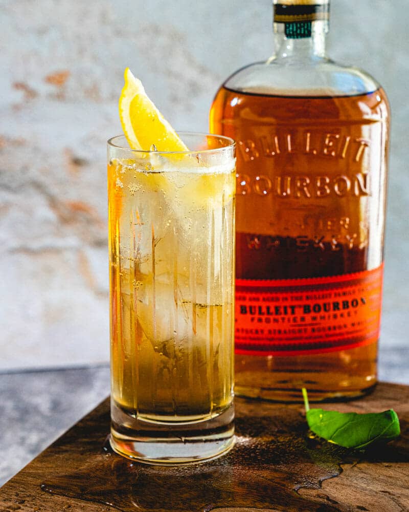 Whiskey highball with lemon slice and bourbon bottle