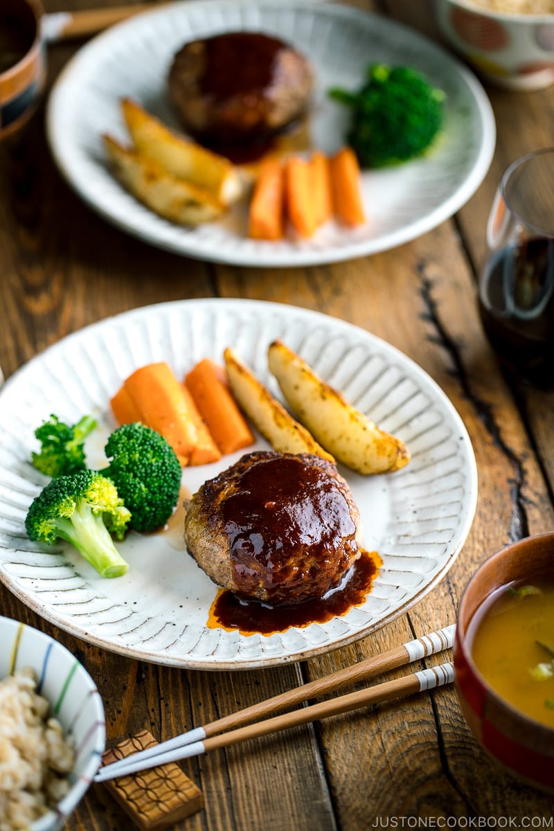 A white plate containing Japanese Hamburger Steak (Hambagu), saut&eacute;ed carrot, broccoli, and baked potato wedges.