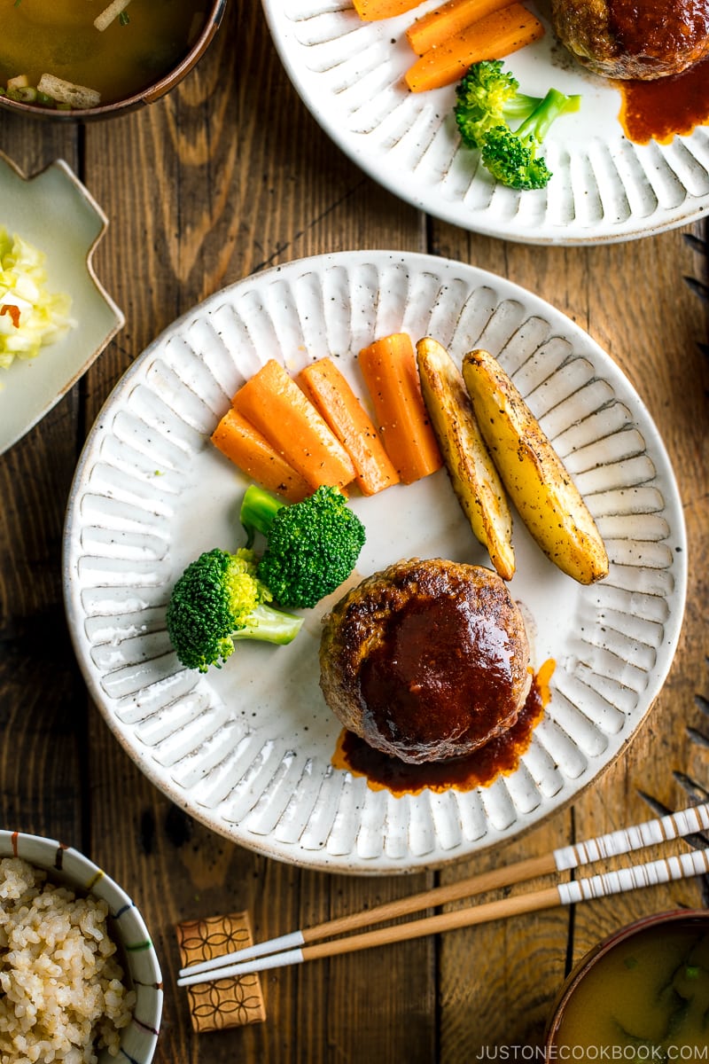 A white plate containing Japanese Hamburger Steak (Hambagu), saut&eacute;ed carrot, broccoli, and baked potato wedges.