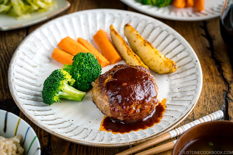 A white plate containing Japanese Hamburger Steak (Hambagu), saut&eacute;ed carrot, broccoli, and baked potato wedges.
