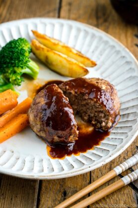 A white plate containing Japanese Hamburger Steak (Hambagu), saut&eacute;ed carrot, broccoli, and baked potato wedges.