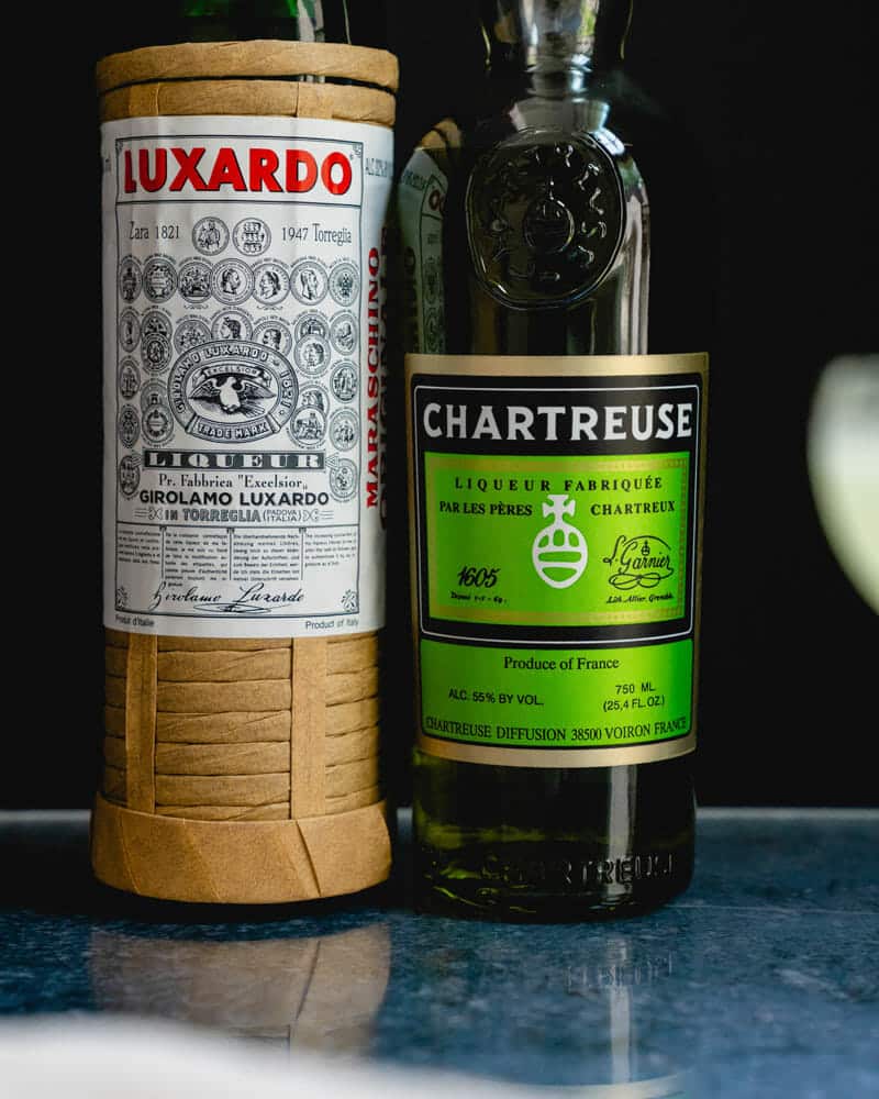A bottle of Luxardo liqueur next to Chartreuse