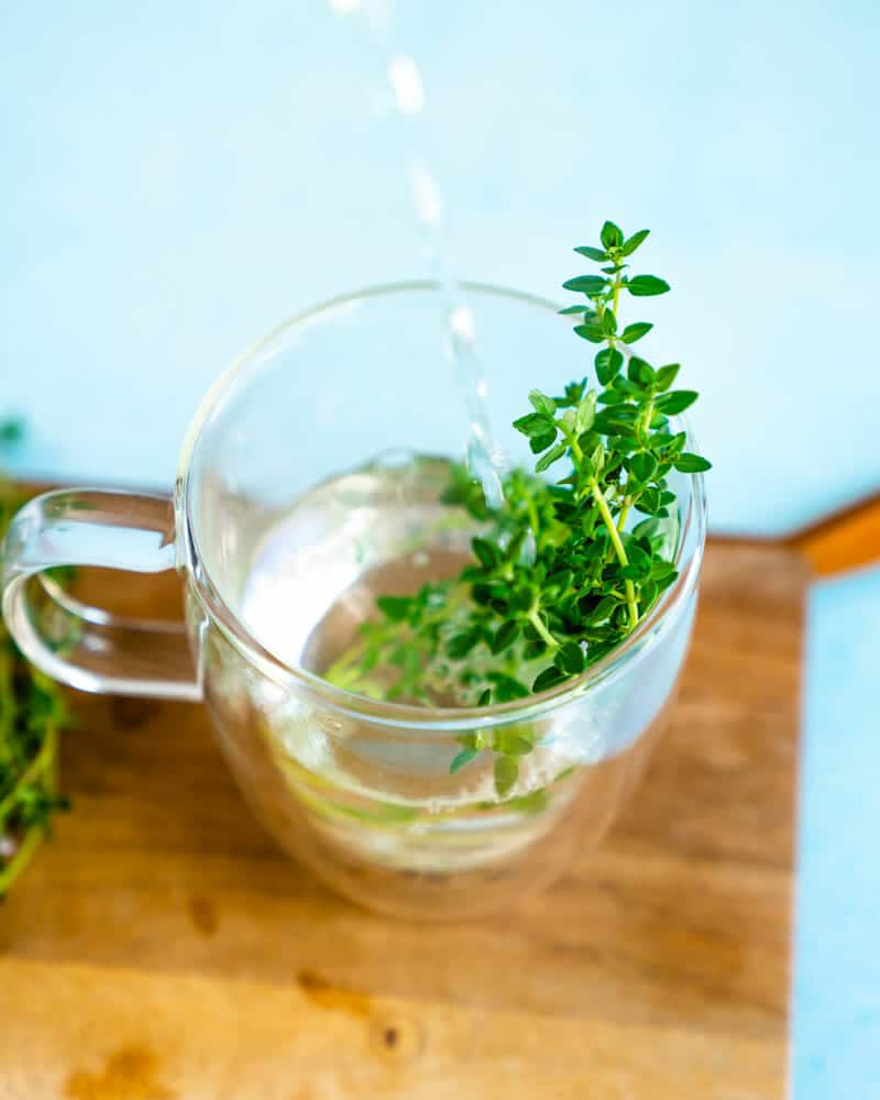 A clear mug with water and thyme