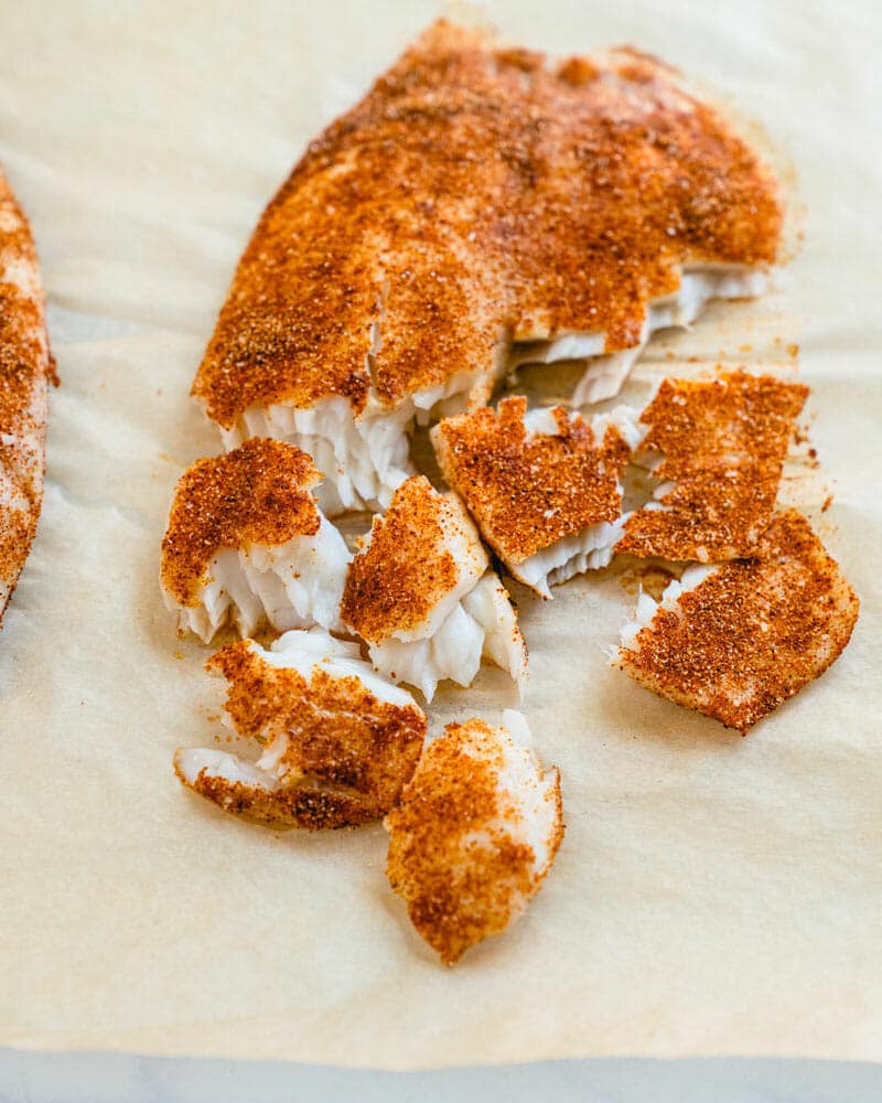 Cooked and seasoned cod with half being broken off into smaller parts for tacos