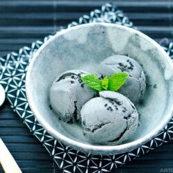 A grey bowl containing Black Sesame Ice Cream garnished with mint on top and sprinkles of black sesame seeds.