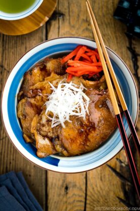 A Japanese bowl containing steamed rice, topped with soy-caramelized pork slices and pickled red ginger.
