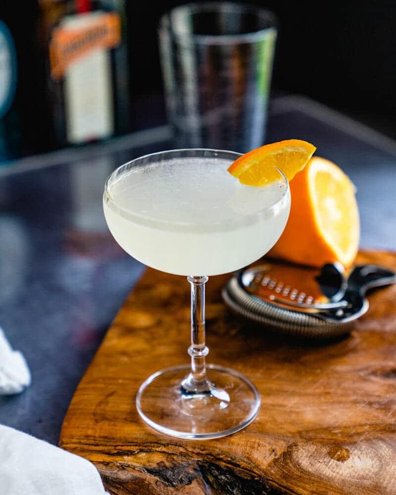Corpse reviver No 2 cocktail in a tall glass and garnished with a lemon wedge with a half cut lemon in the background