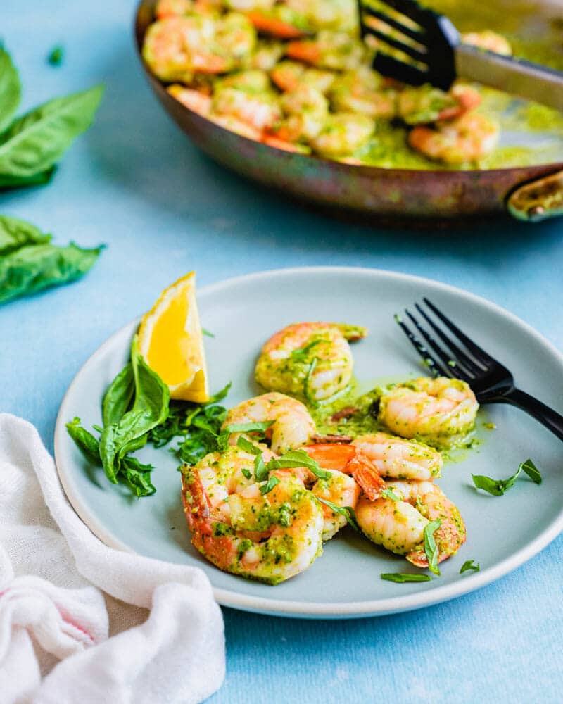 Shrimp in pesto sauce on a plate with a lemon wedge 