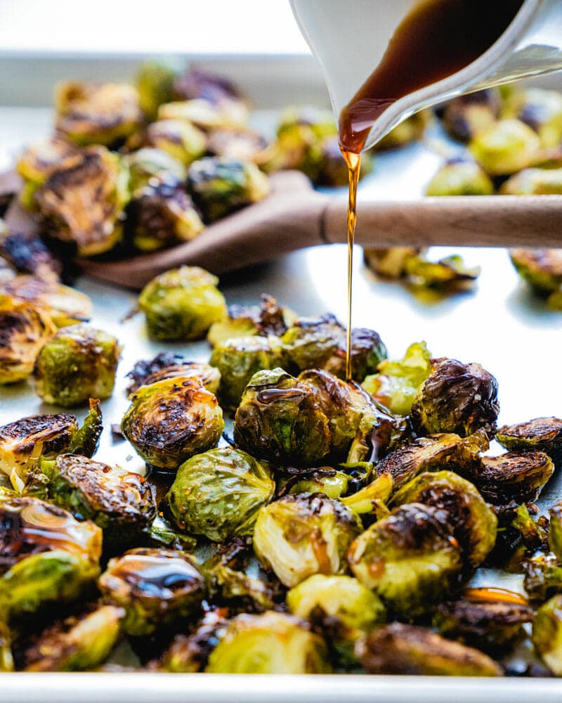 Crispy roasted brussels sprouts being drizzled with a mape glaze