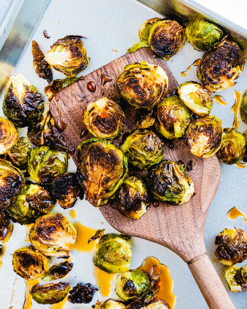 Crispy cooked brussels sprouts in a maple glaze being scooped up by a wooden spatula