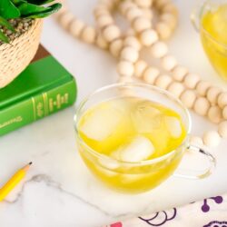 green iced tea in a glass cup on top of marble table next to a book and a plant