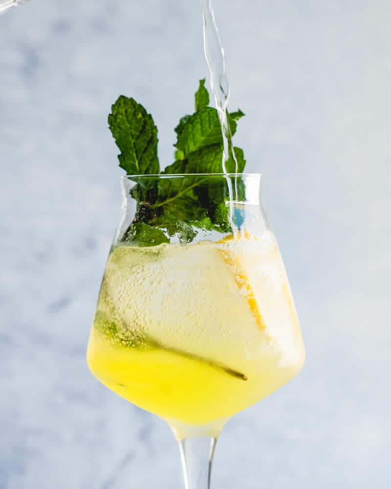 Limoncello spritz and mint garnish in a stemmed glass with Limoncello being poured in