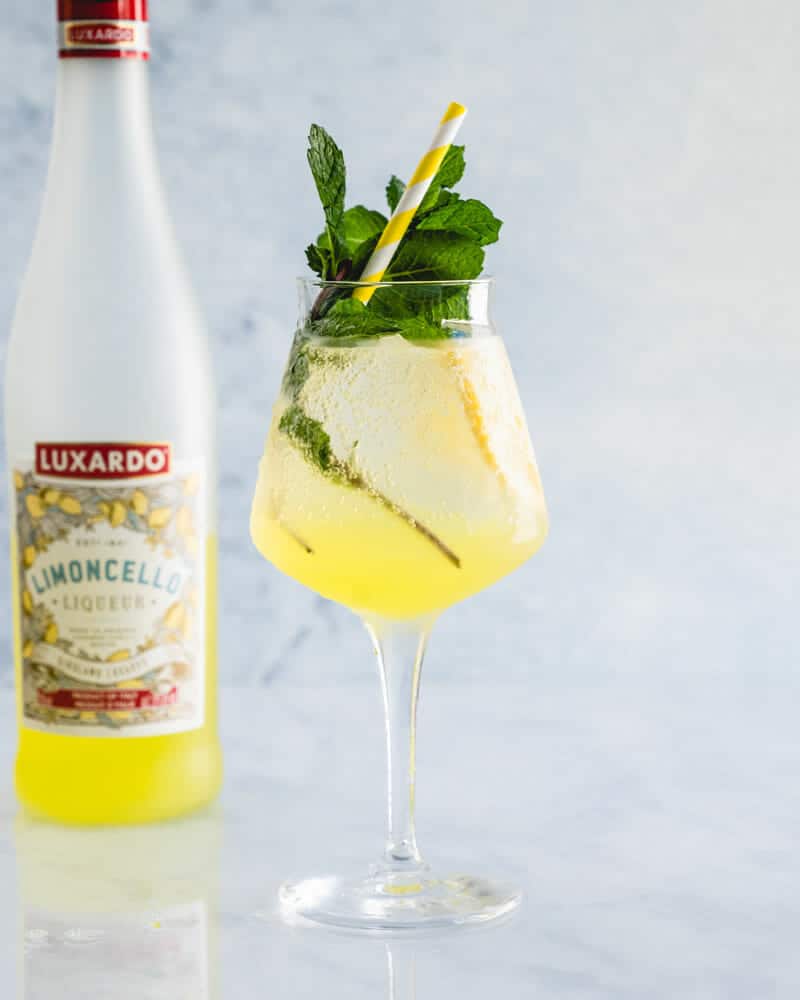 Limoncello spritz in a stemmed glass with mint and a straw next to a bottle of Limoncello