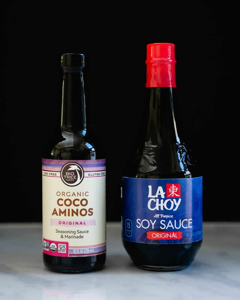 A bottle of Big Tree Organic Coco Aminos Original and a bottle of La Choy All Purpose Soy Sauce Original sitting on a table next to each other
