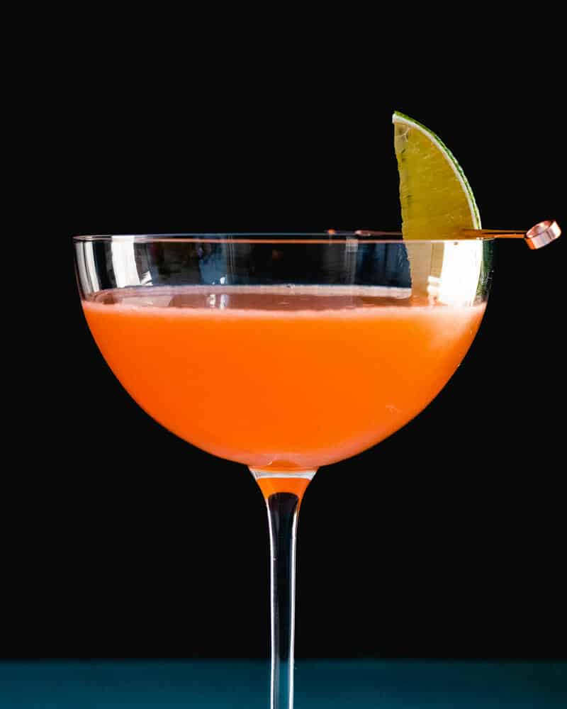 Naked and Famous cocktail in a tall cocktail glass, garnished with lime
