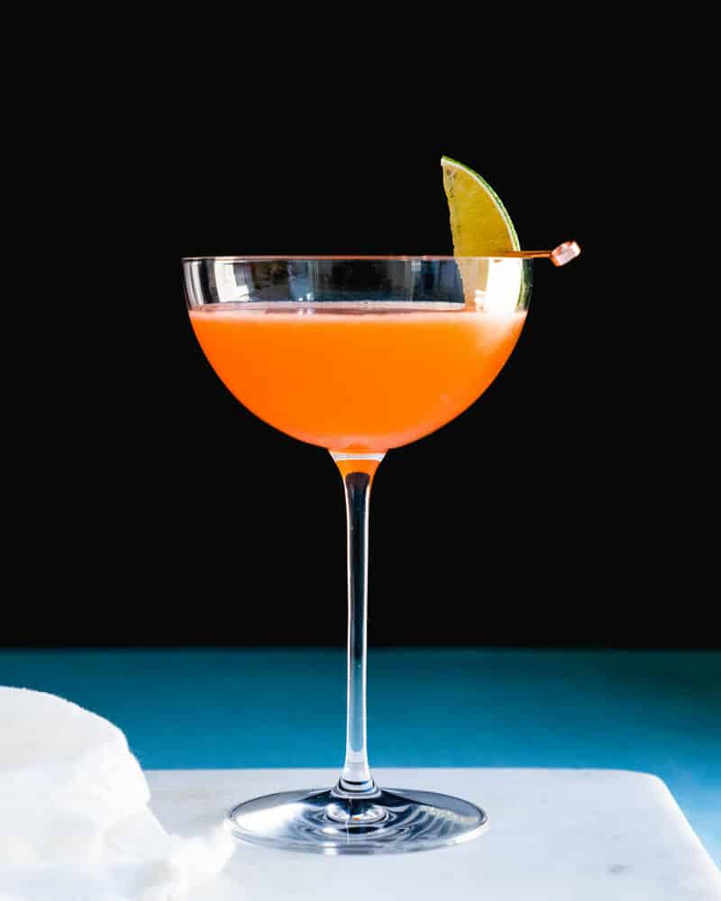 Naked and Famous cocktail in a tall cocktail glass, garnished with lime