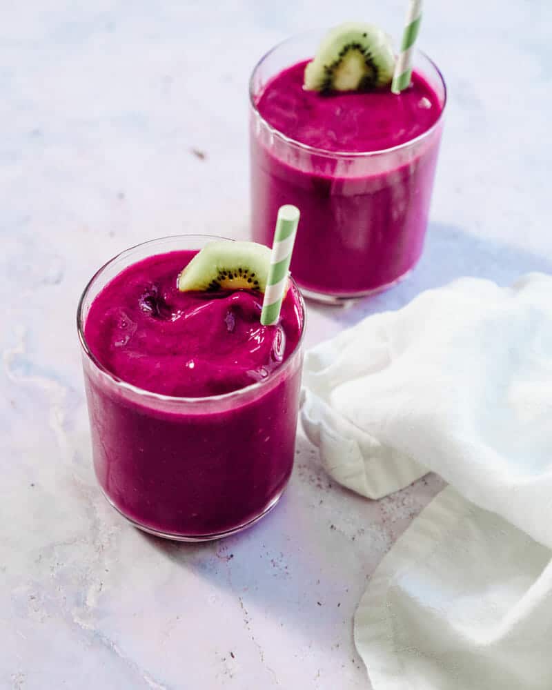 Two pink dragon fruit smoothie in a cup with a colorful straw and garnished with a kiwi
