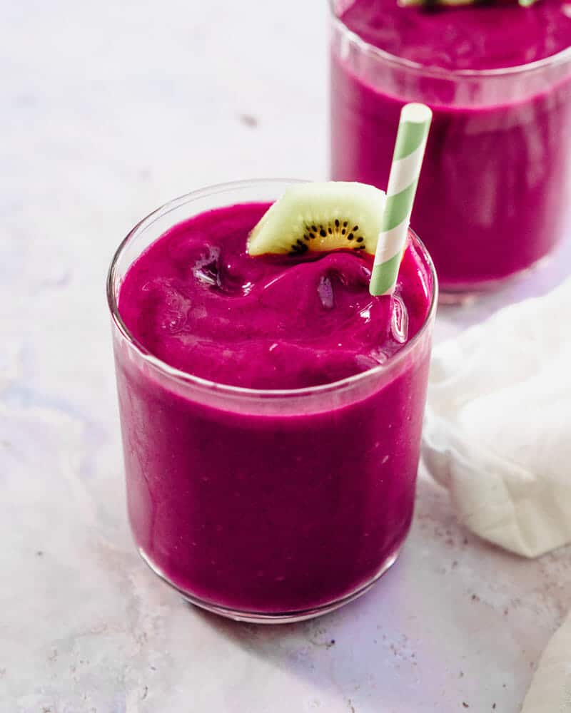 Pink dragon fruit smoothie in a cup with a colorful straw and garnished with a kiwi