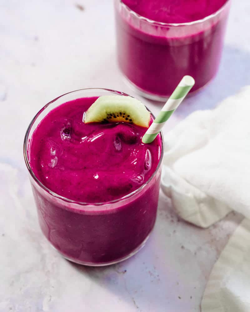 Pink dragon fruit smoothie in a cup with a colorful straw and garnished with a kiwi