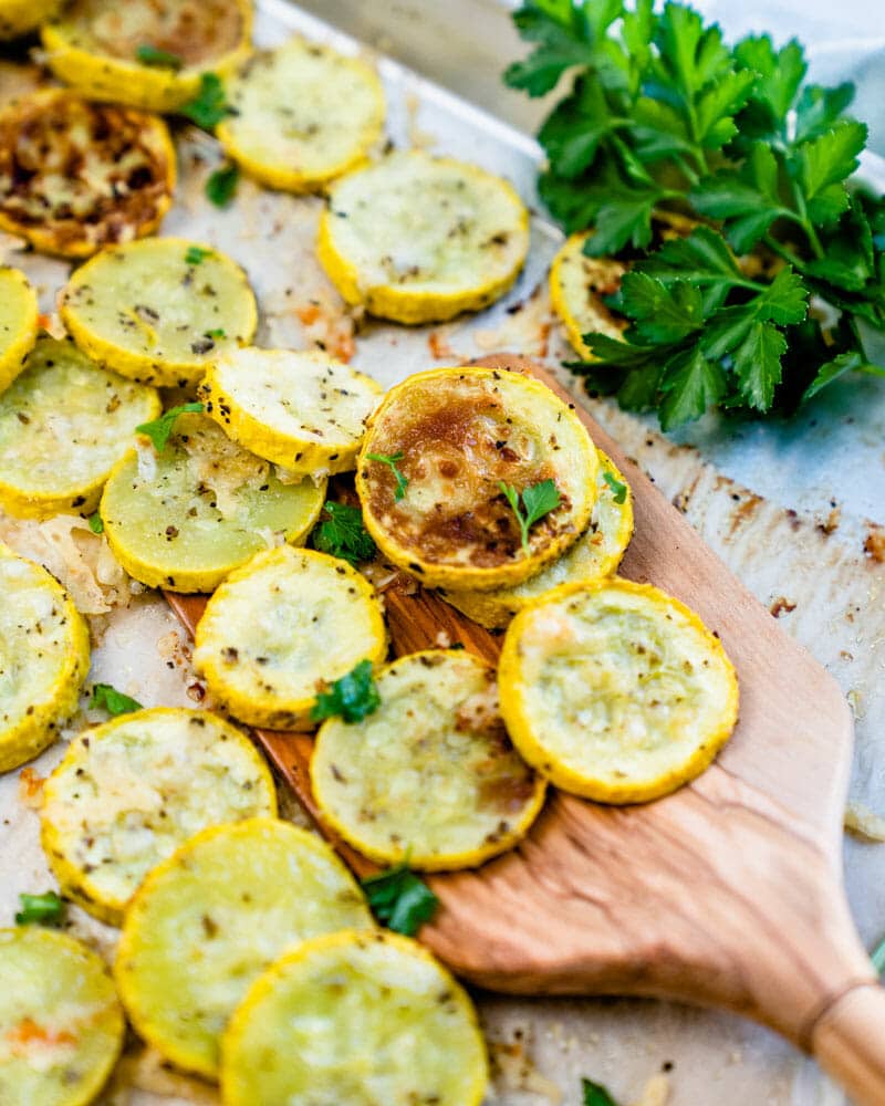 Roasted yellow squash sliced, cooked, and seasoned, sitting on a cutting board with herbs 