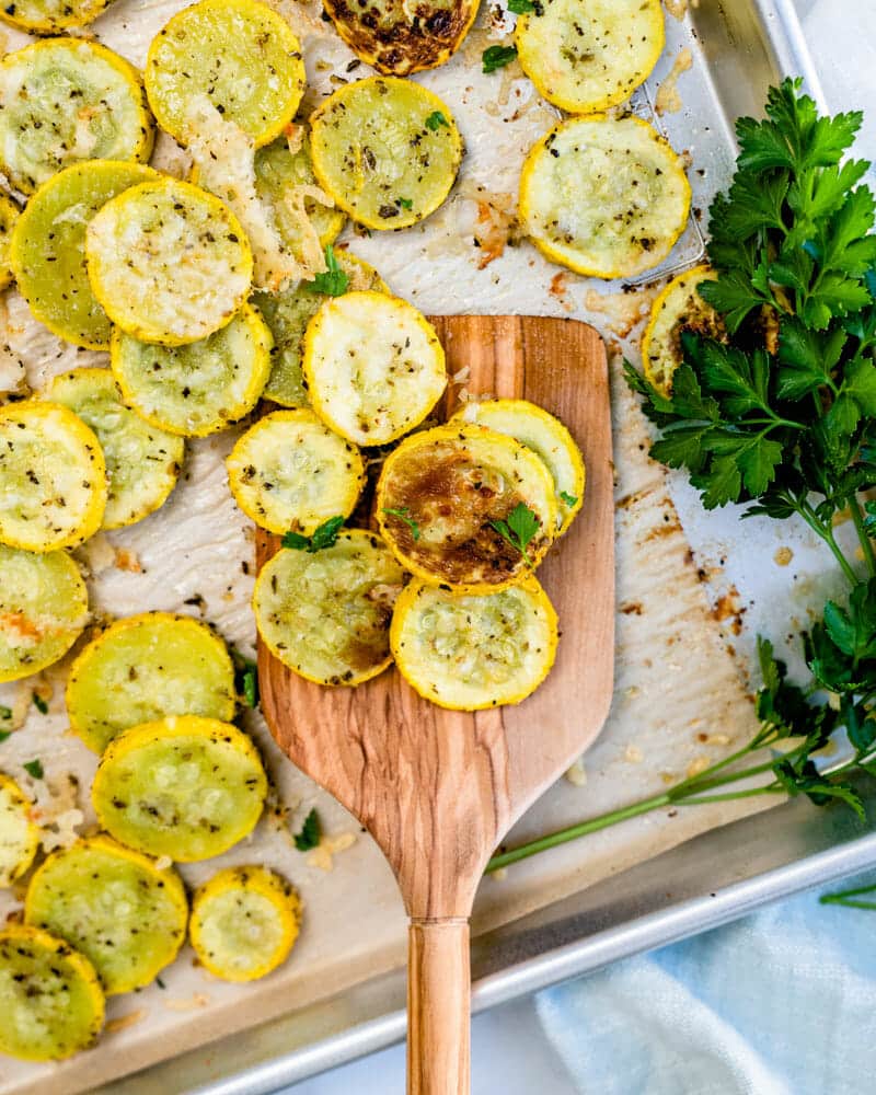 Roasted yellow squash sliced, cooked, and seasoned, sitting on a cutting board with herbs 
