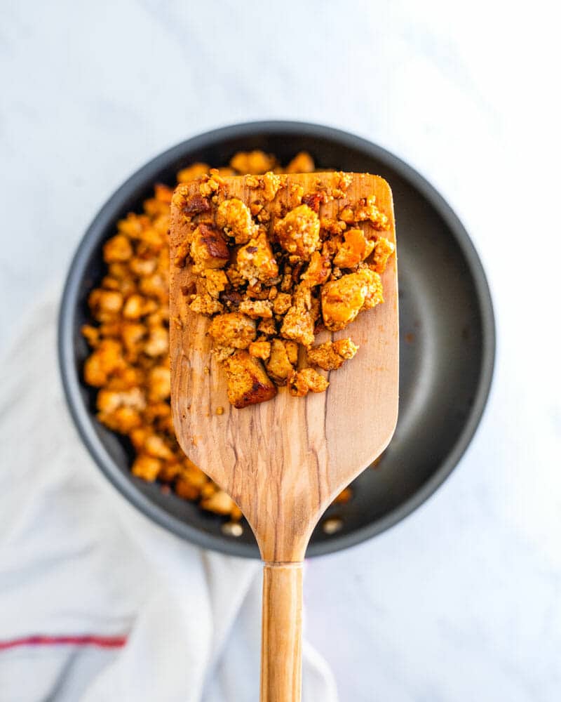 Tofu tacos crumbles on a wooden cooking utensil over a pan of crumbles in the background
