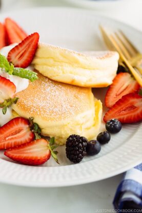 A white plate containing fluffy Japanese souffl&eacute; pancakes and berries.
